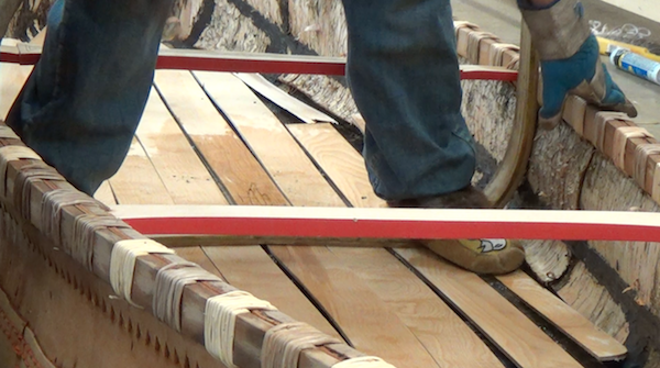 Wayne uses his feet, fitted with mocassins to finish the bending in the canoe.  The rib is bent into the proper shape while others hold sides of canoe